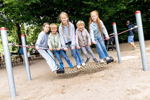 Fünf Kinder nebeneinander auf länglicher, seitwärts schwingender Schaukel