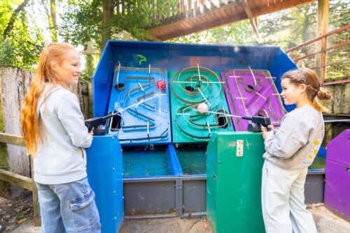 Zwei Mädchen schießen mit Wasserpistolen auf jeweils einen Ball in einer Spur an der Zielwand