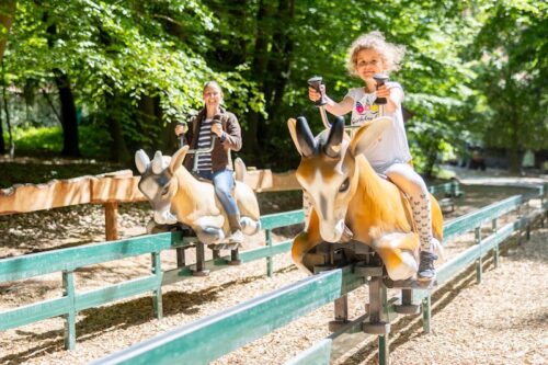 Mutter und Kind auf jeweils einer Ziegenfigur sitzend und um die Wette fahrend