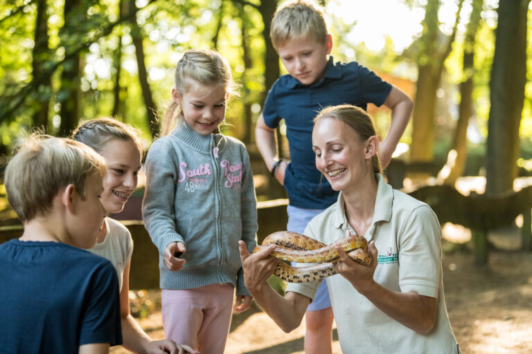 Eine Gruppe Kinder steht um eine Pädagoging mit Schlange in der Hand